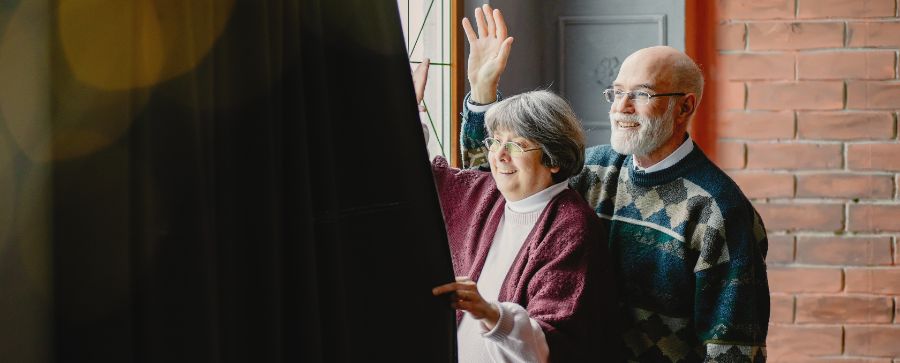 Dos personas mayores dentro de un apartamento saludando